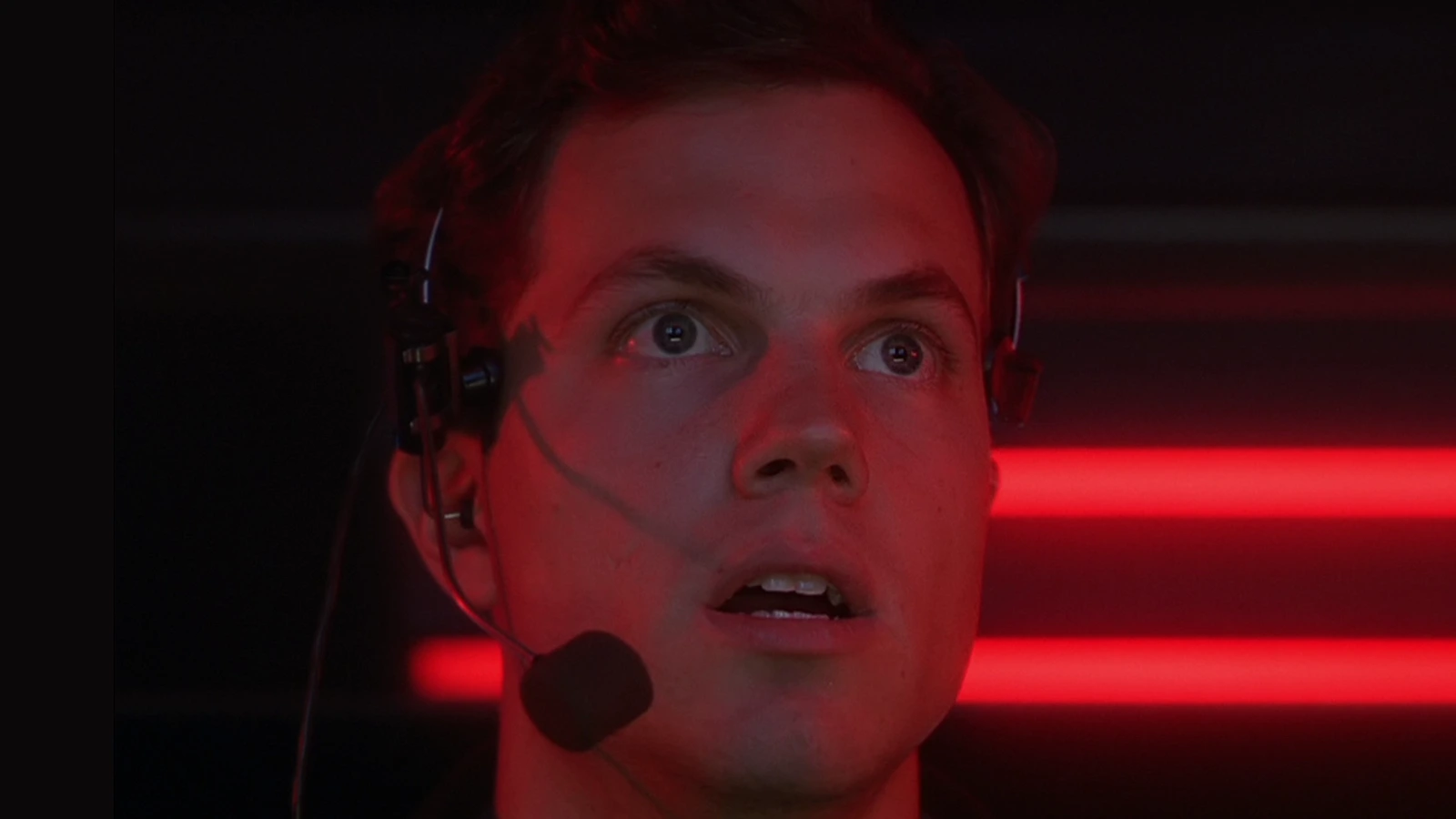 Garber wearing a headset and staring up at the monitors under red light in the OWLF command trailer in Predator 2