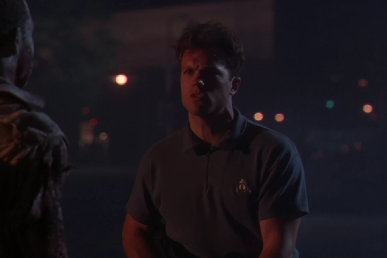 Garber in a dark polo shirt facing another man on a dark street at night in Predator 2