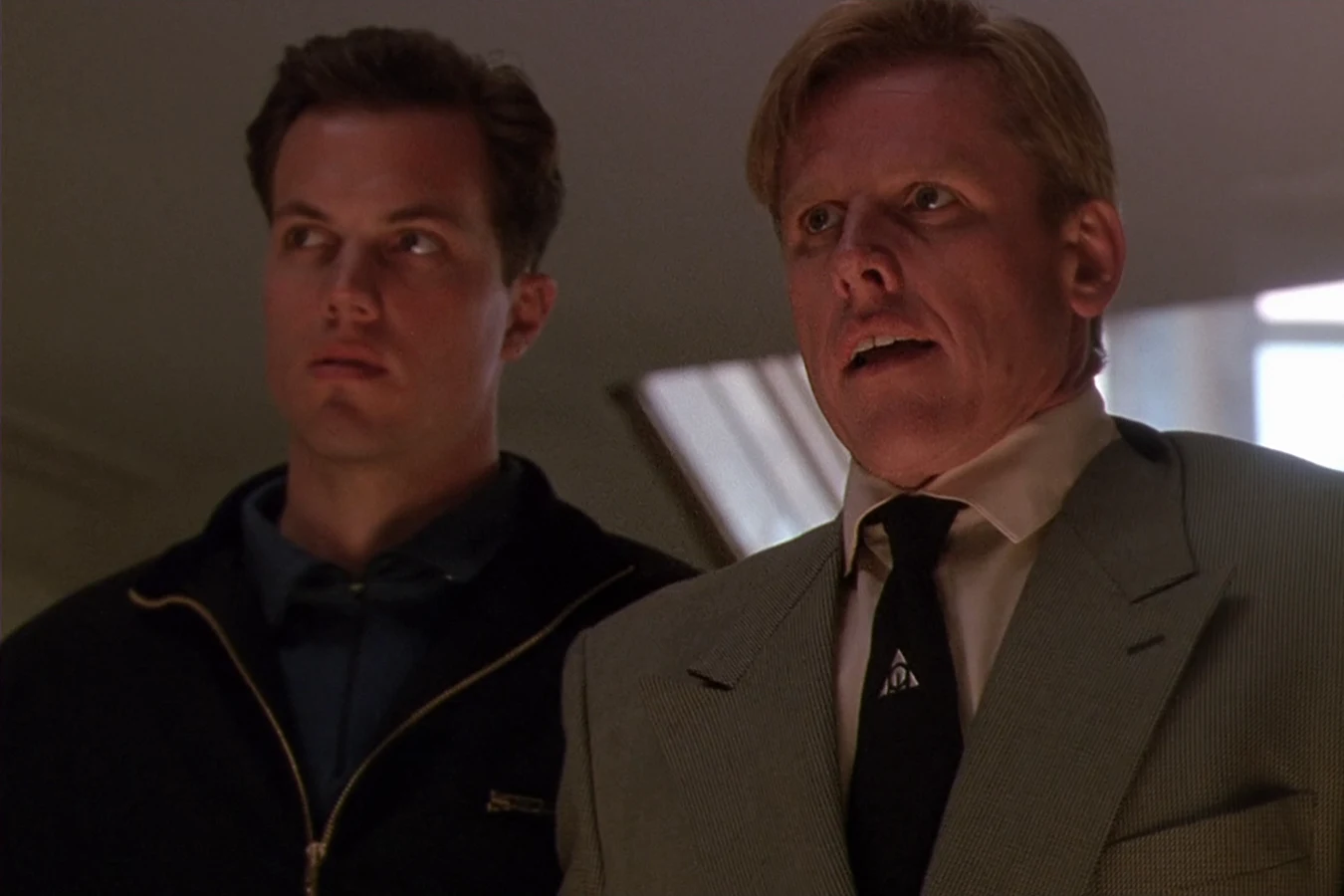 Garber standing beside Peter Keyes in a grey suit as both men look up in Predator 2