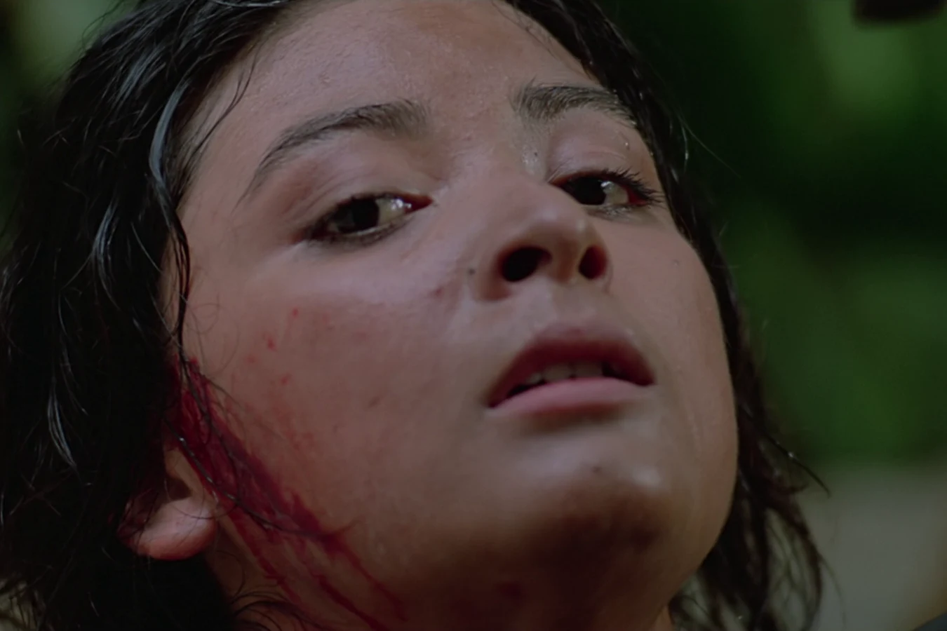 Close-up of Anna Gonsalves looking up with blood on her face as she remembers the demon of her childhood