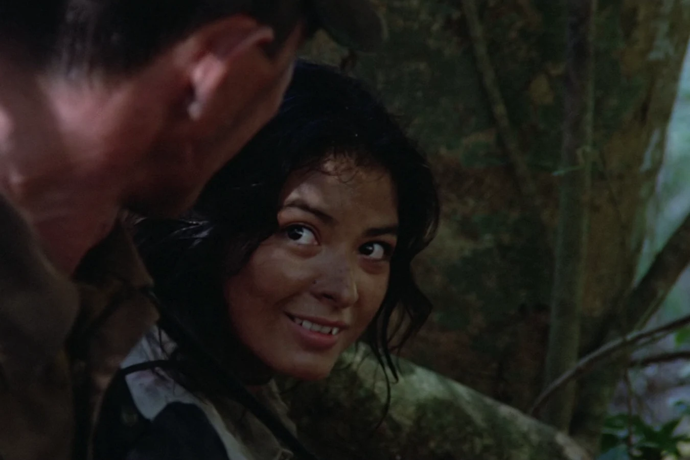 Anna Gonsalves glancing back with a defiant smile as one of the commandos leans over her in the jungle