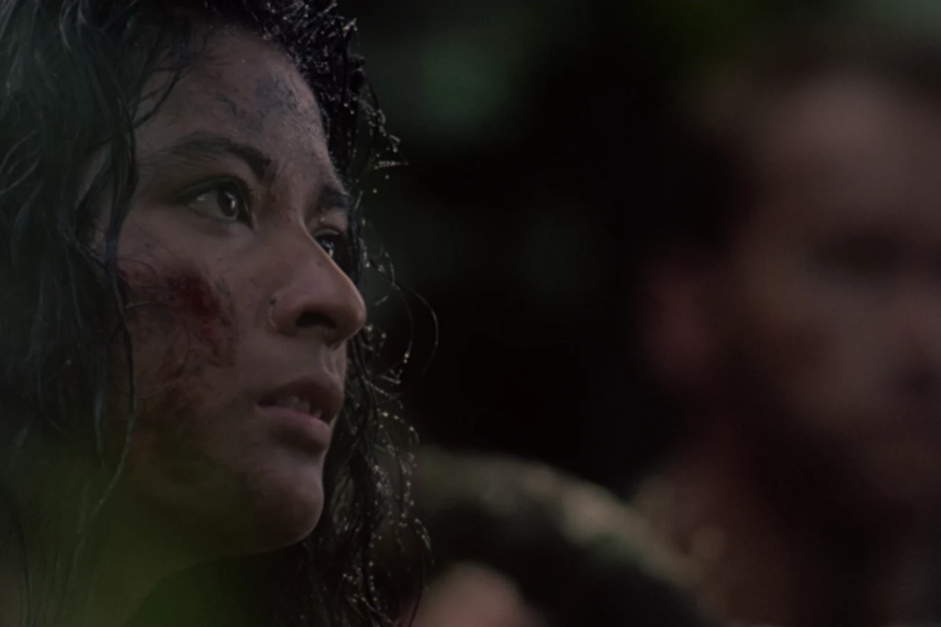 Anna Gonsalves in the dark jungle at night, her face lit faintly and streaked with blood