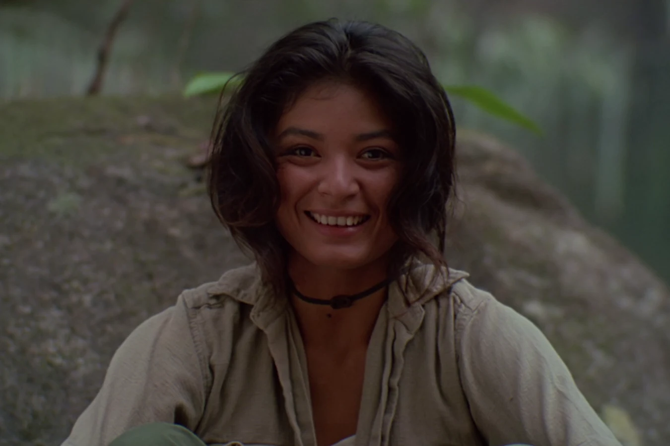 Anna Gonsalves smiling as she sits by a large rock in the jungle