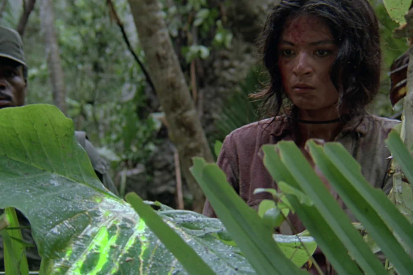 Anna Gonsalves making her way through thick jungle leaves with a commando behind her