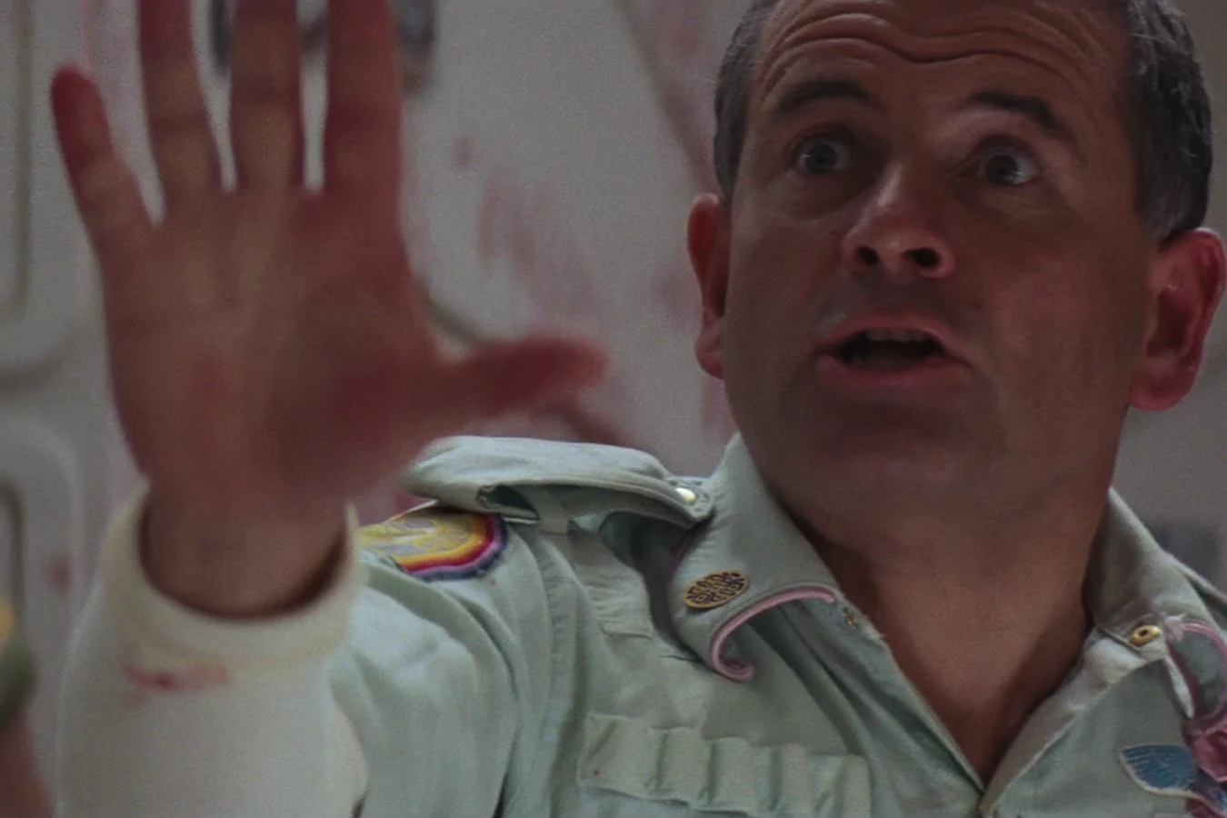 Ash raising a hand at the Nostromo mess table as Kane seized