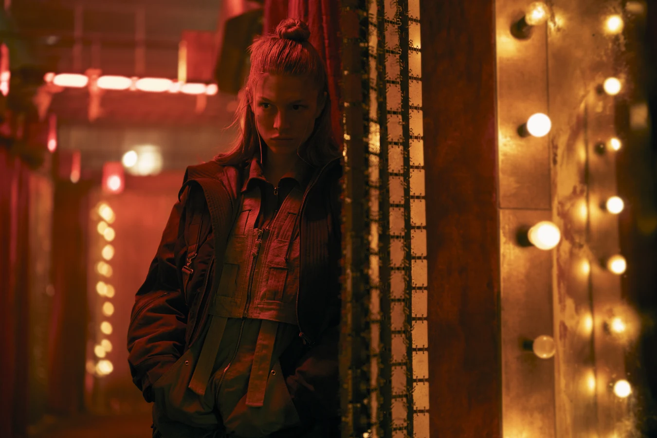 Hunter Schafer as Cora standing in a red corridor lined with bulbs in Blade Runner 2099
