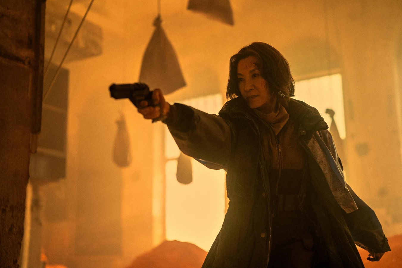 Michelle Yeoh as Olwen aiming a pistol in amber haze in Blade Runner 2099