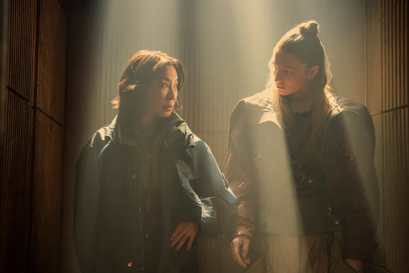 Michelle Yeoh as Olwen and Hunter Schafer as Cora standing in a shaft of light in Blade Runner 2099