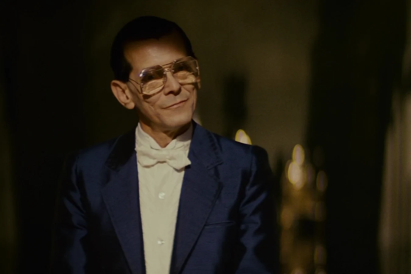 Eldon Tyrell smiling in his dark office in a blue suit and white bow tie in Blade Runner (1982)