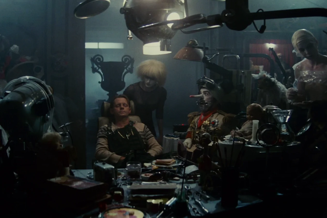 J.F. Sebastian resting with his eyes closed at his cluttered table as Pris stands behind him and his toy Kaiser sits nearby in Blade Runner