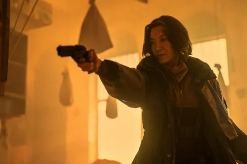 Michelle Yeoh as Olwen aiming a pistol in amber light in Blade Runner 2099
