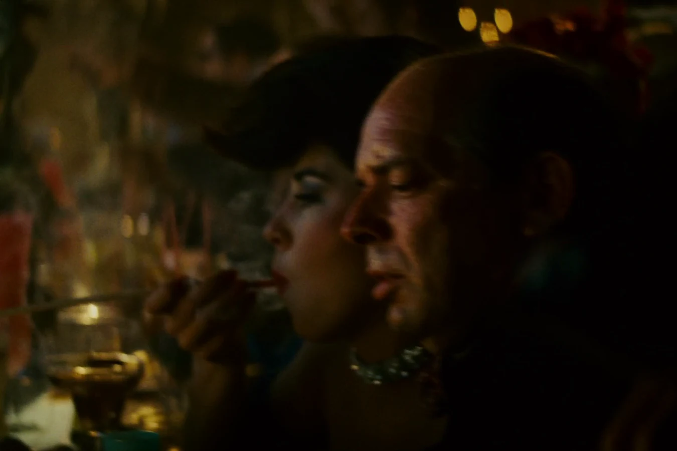 A woman smoking a long pipe beside a bald patron at the candlelit Snake Pit bar in Blade Runner
