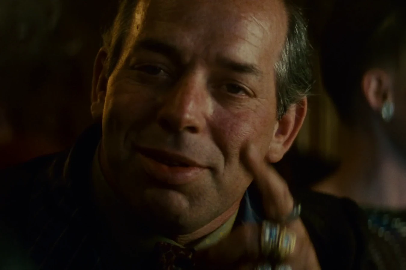 Hy Pyke as Taffey Lewis smiling with a ringed hand raised to his face at his bar in Blade Runner