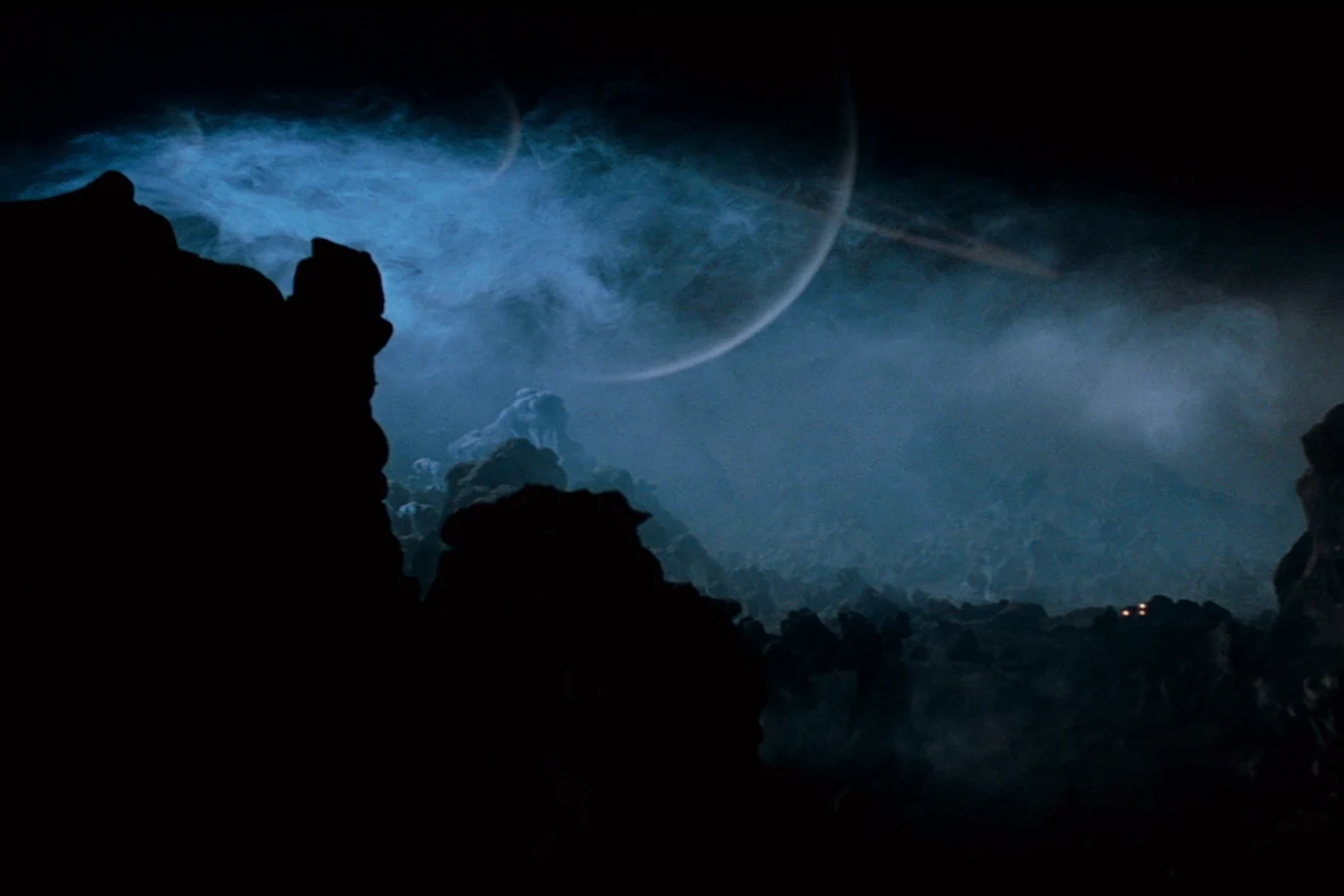 The crescent and ring of Calpamos through the storm clouds above the rocks on LV-426 in Alien