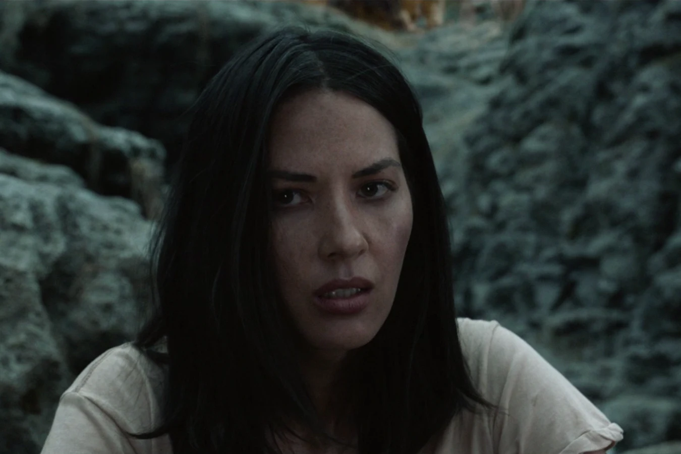 Close-up of Casey Brackett among dark rocks in the forest, her face dirty after the fight