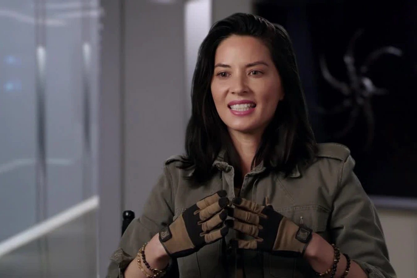 Olivia Munn in Casey Brackett's olive field jacket and fingerless gloves during an interview for The Predator
