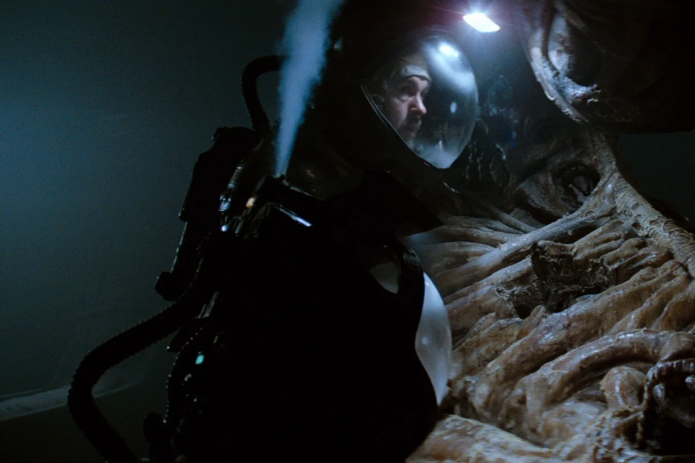 Dallas in a helmet beside the fossilized Space Jockey in the derelict