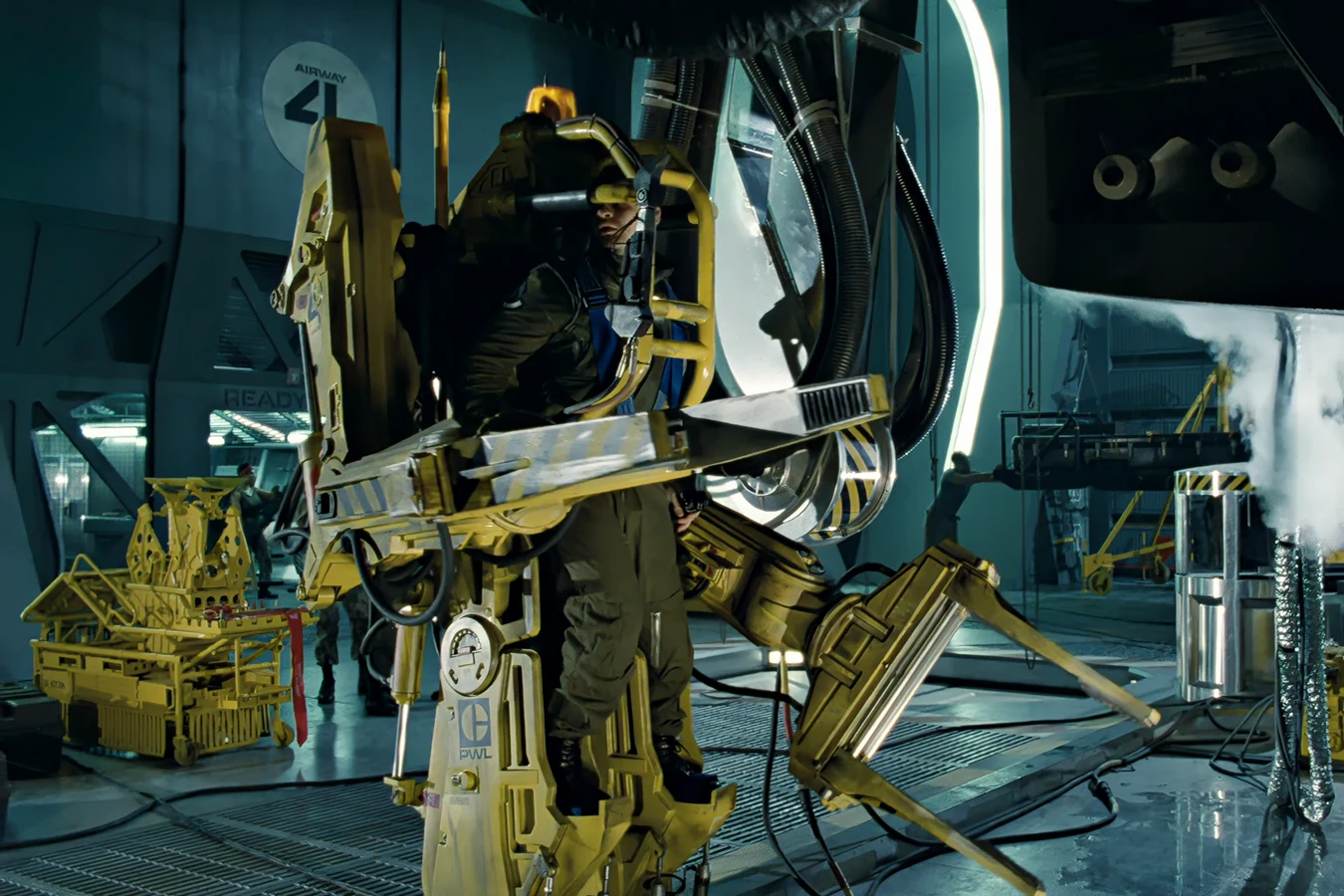 Daniel Spunkmeyer in a yellow P-5000 Power Loader on the Sulaco hangar deck in Aliens, with Airway 41 on the wall behind him