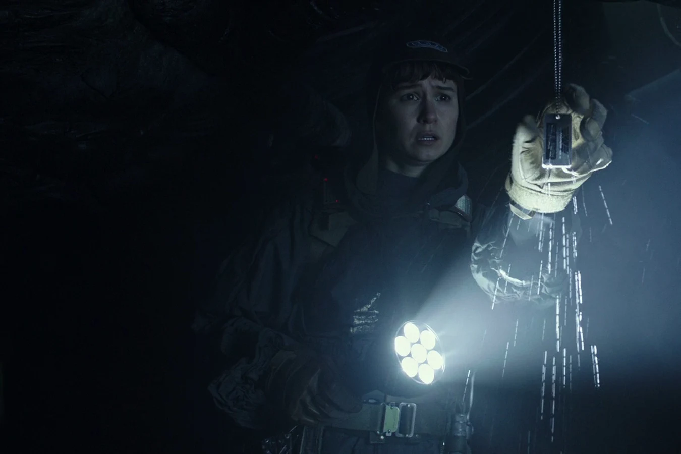 Daniels inside the crashed Juggernaut, holding Dr. E. Shaw's dog tags in a flashlight beam