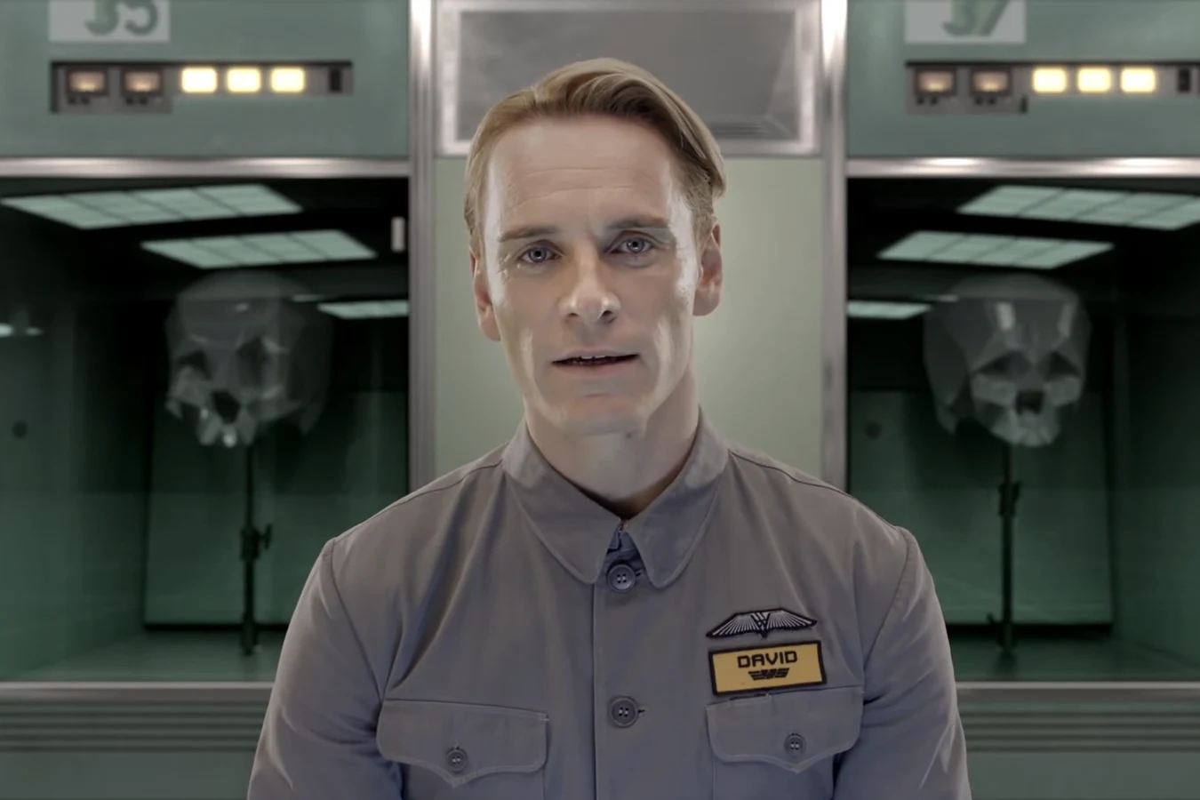 David in a grey Weyland uniform with his name badge, speaking to the camera in the Weyland Corp advertisement
