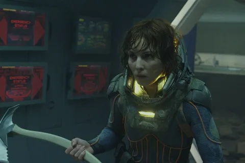 Elizabeth Shaw in a damaged spacesuit on the lifeboat, holding a fire axe under red emergency screens