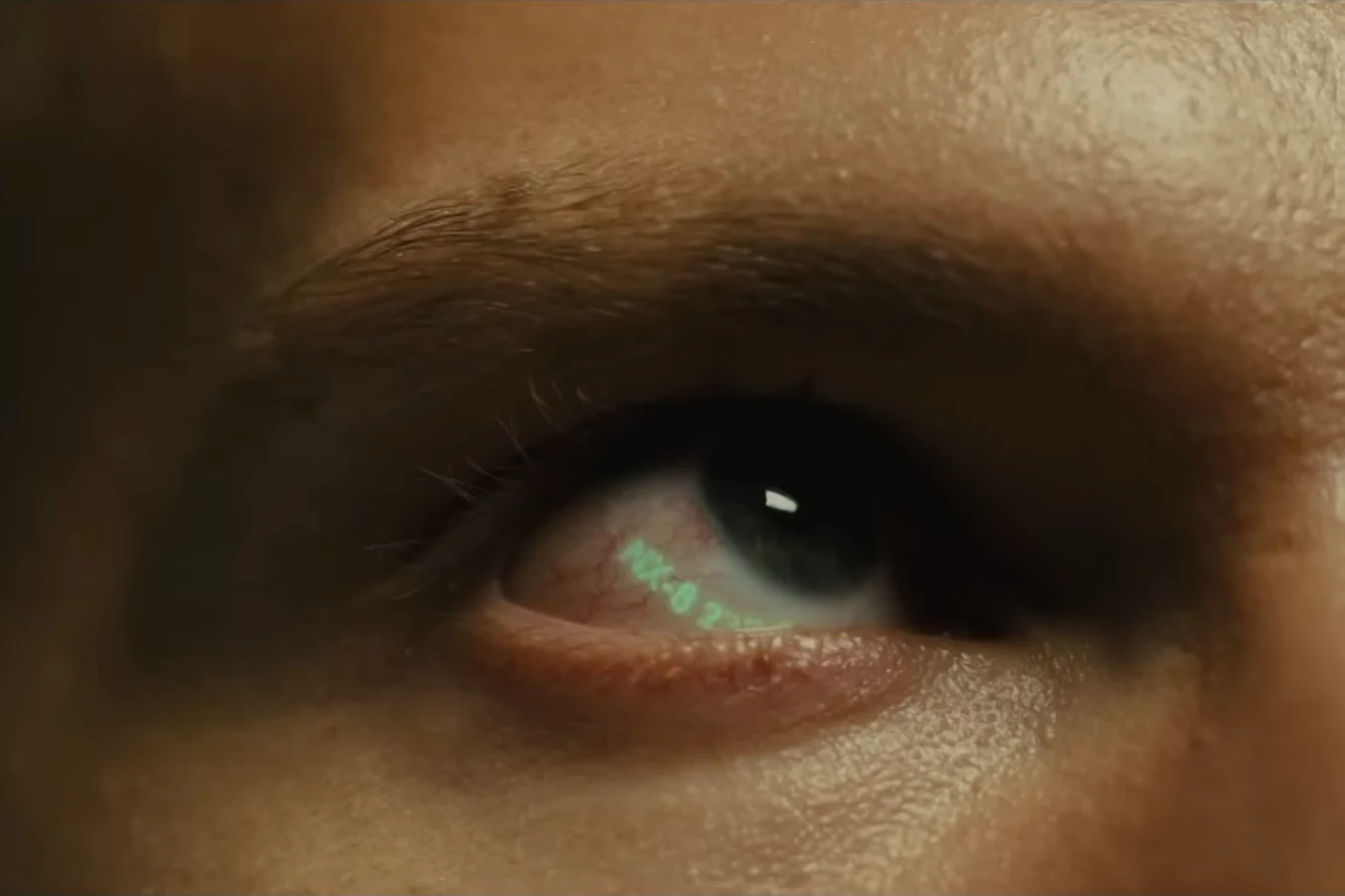 An extreme close-up of the Nexus-9 replicant's eye with a green serial number glowing in it in 2036: Nexus Dawn
