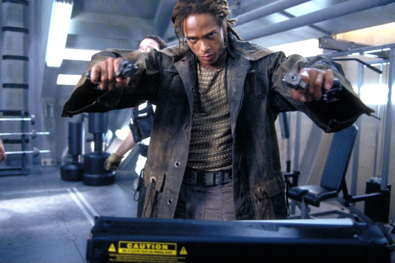 Gary Dourdan as Christie holding out both pistols on the Auriga gym set in a production still from Alien: Resurrection