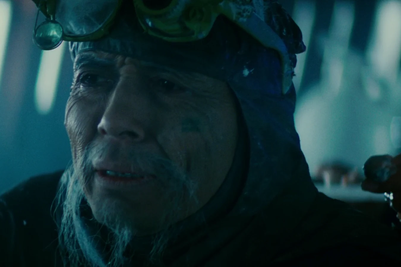Chew without his fur coat, frost on his face, as a hand reaches over his shoulder in the eye lab in Blade Runner