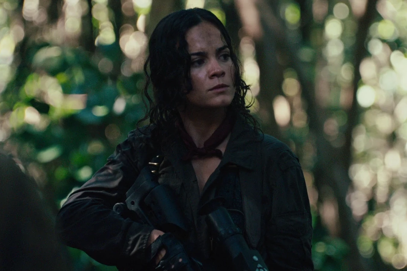 Isabelle holding her rifle low as she moves through bright green jungle undergrowth