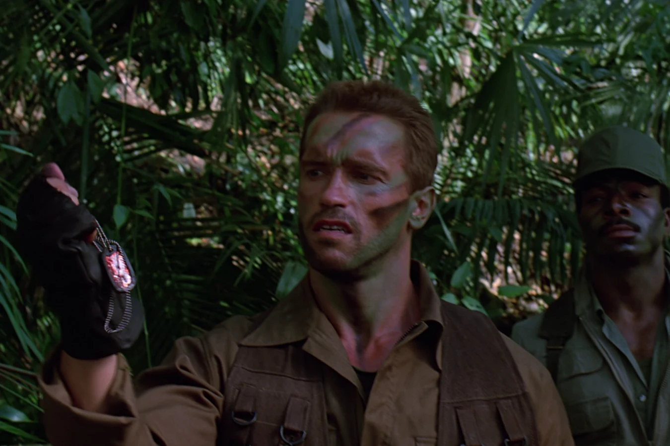 Dutch Schaefer holding Hopper's dog tags in the jungle in Predator