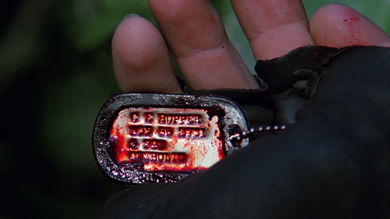 Close-up of Hopper's bloody dog tags in a gloved hand in Predator