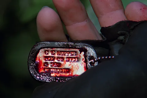 Close-up of Hopper's bloody dog tags in a gloved hand in Predator