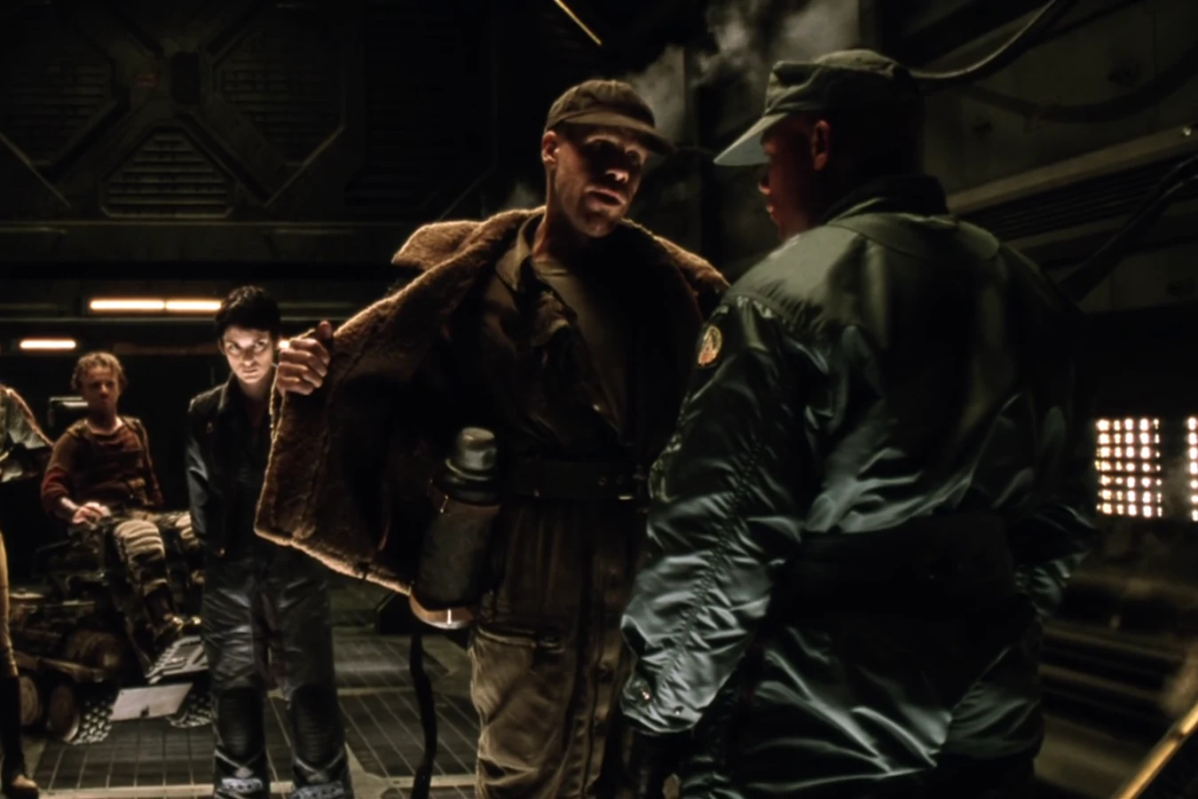 Johner opening his coat for a USM weapons search on the Auriga, with Call and Vriess behind him