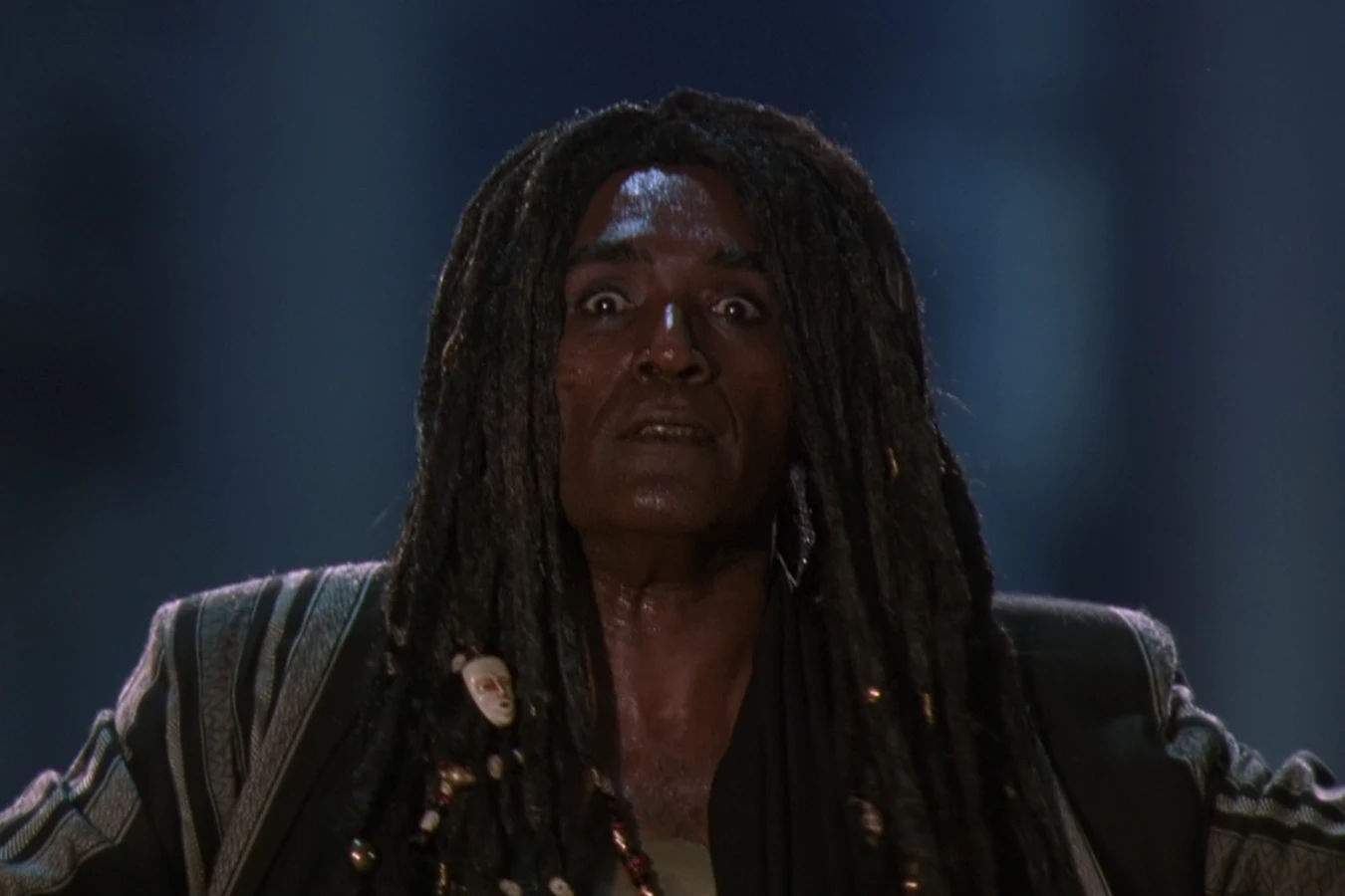 King Willie spreads his arms wide in his striped coat and dreadlocks in the alley in Predator 2
