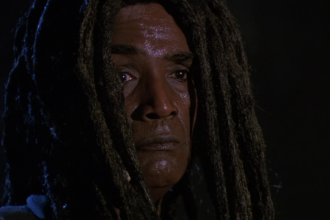 King Willie's scarred face framed by dreadlocks in the dark in Predator 2