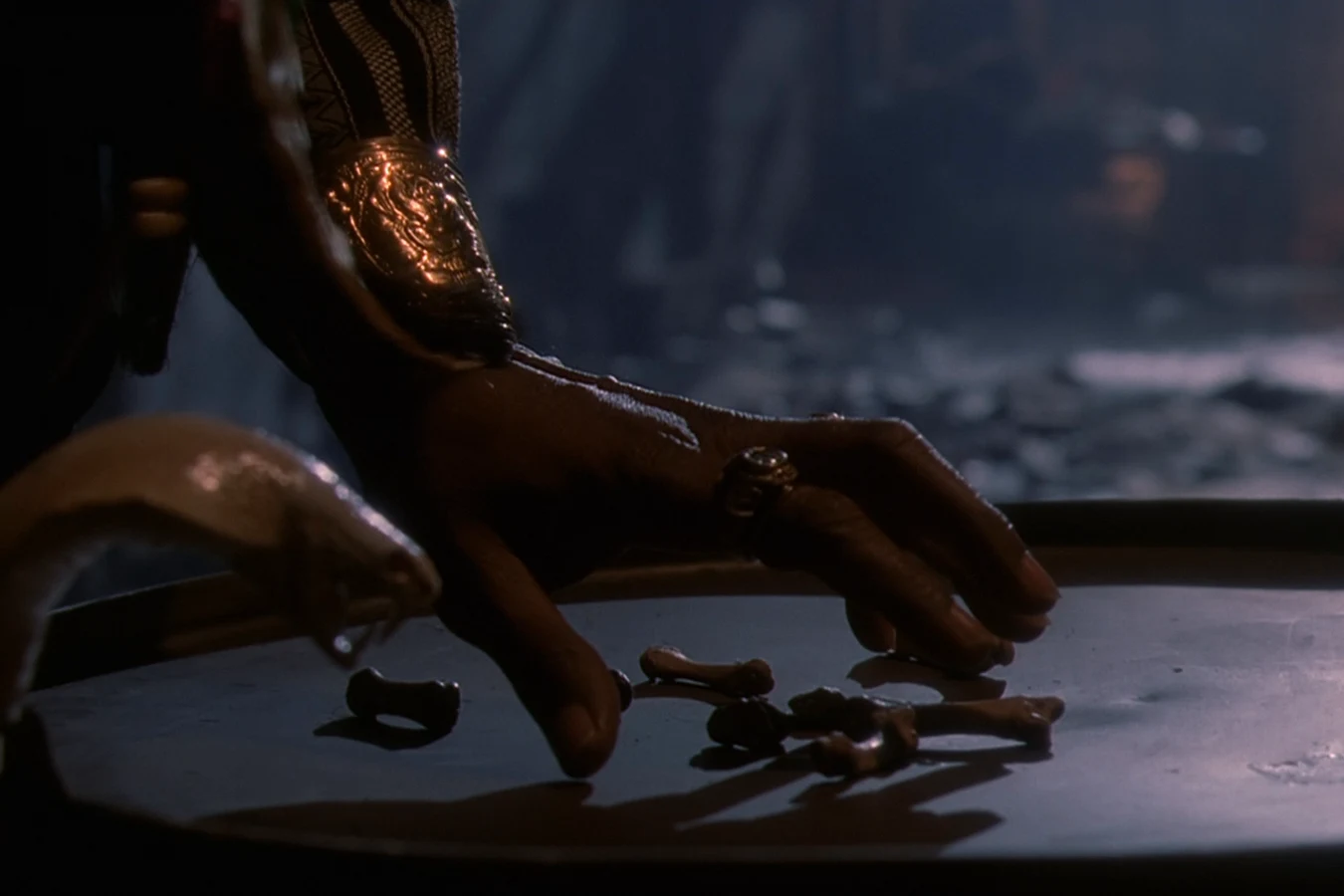 King Willie casts small bones across a crate lid in the alley in Predator 2