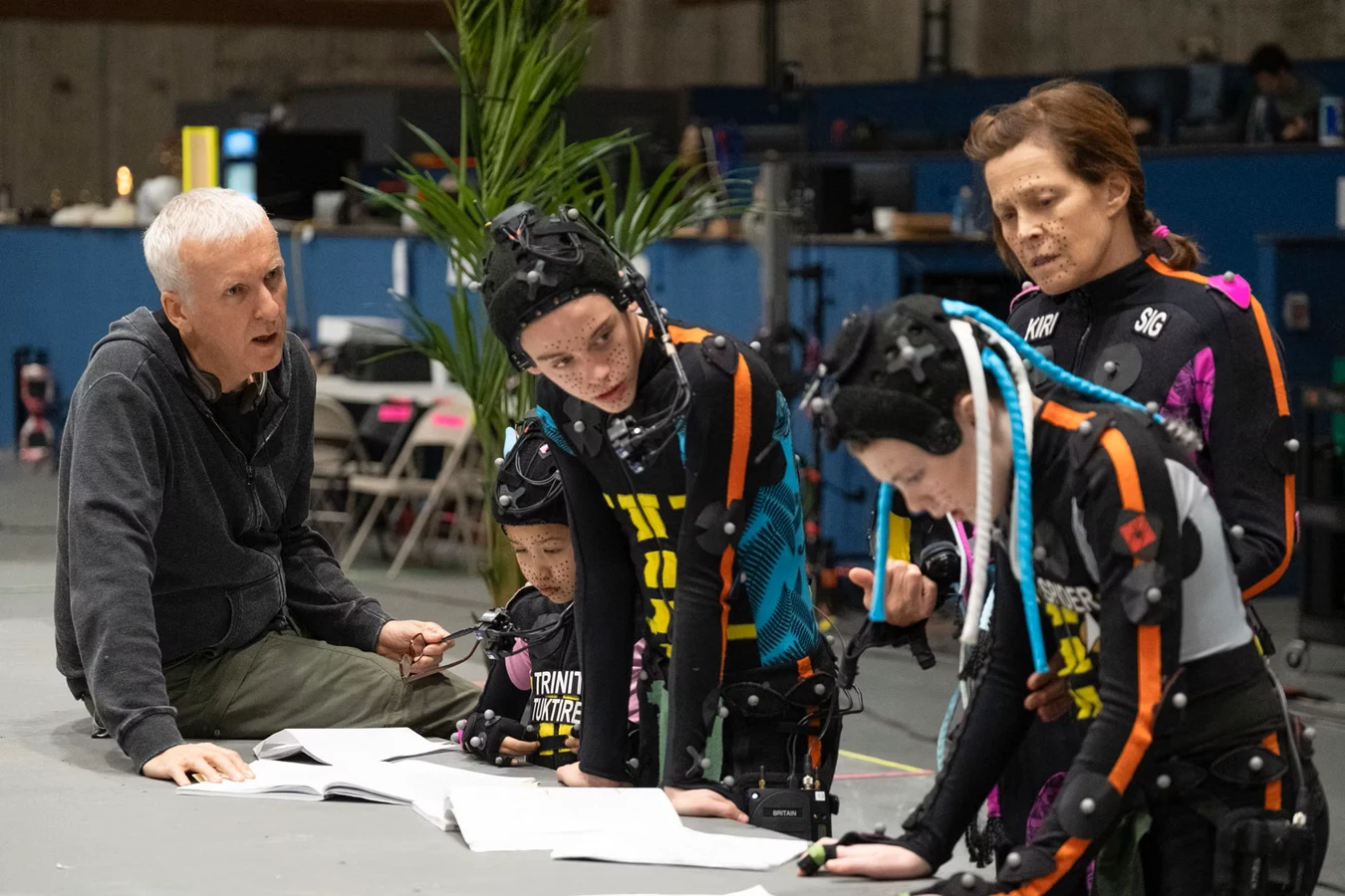 James Cameron reviewing scripts on the volume floor with Sigourney Weaver in a Kiri marker suit and the young Avatar cast