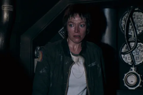 Lambert in a green jacket stands in a Nostromo corridor in Alien