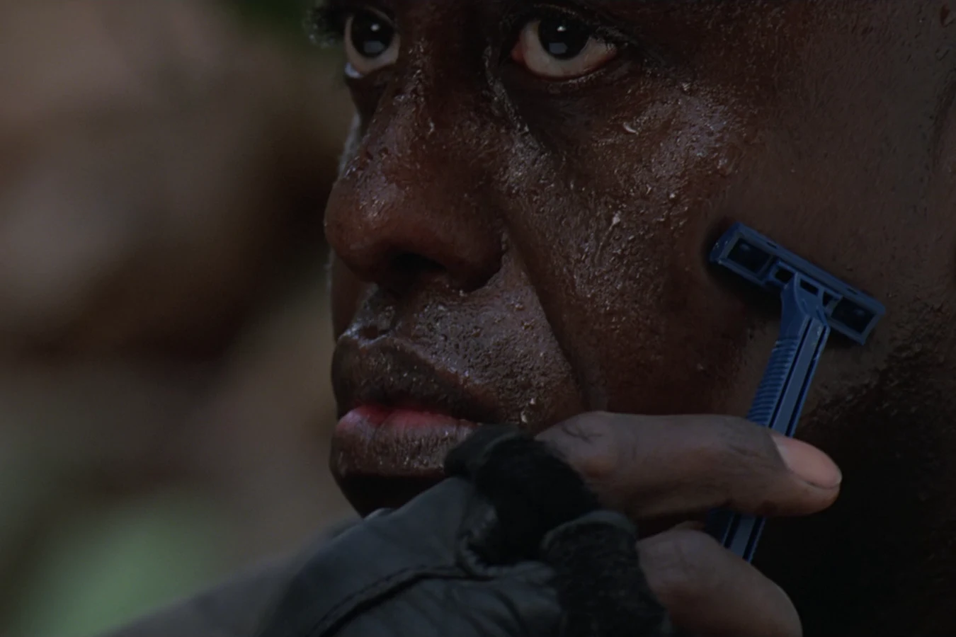 Mac Eliot dry-shaving his face with a disposable razor in the jungle in Predator