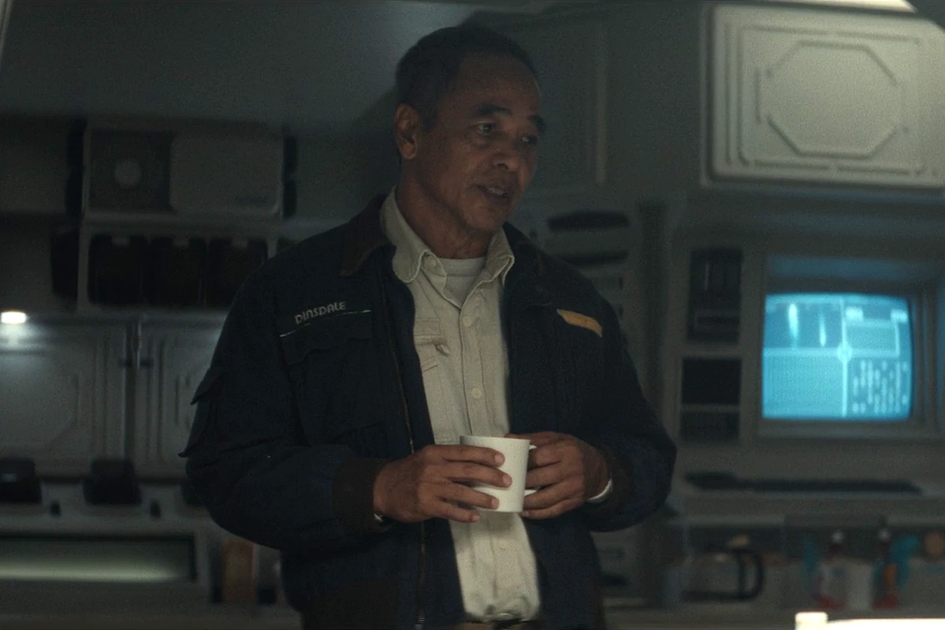 Captain RJ Dinsdale holding a mug in his Maginot jacket in the mess hall in Alien: Earth