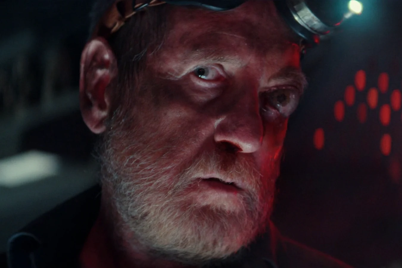 Close-up of Shmuel lit in red with a headlamp on his brow aboard the Maginot in Alien: Earth