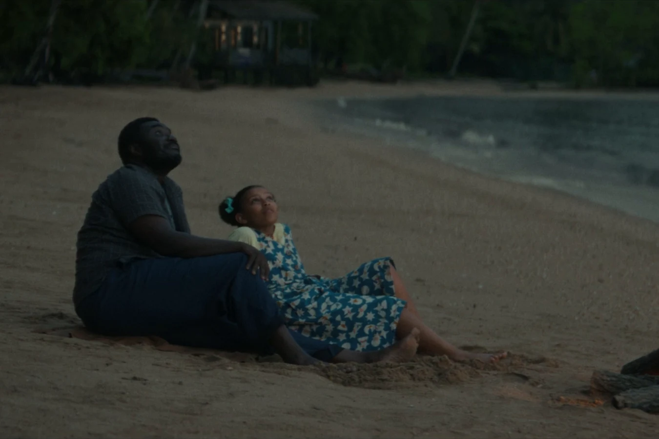 Morrow sitting on a beach at dusk beside his young daughter Estelle and a campfire in Alien: Earth