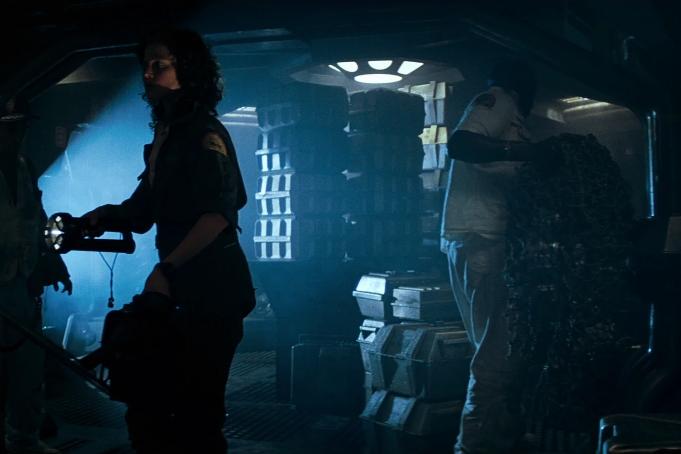 Parker holds a capture net in a cargo bay while Ripley carries a flamethrower on the Nostromo