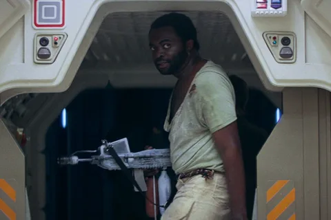 Parker in a torn undershirt carries a weapon through a Nostromo hatch in Alien