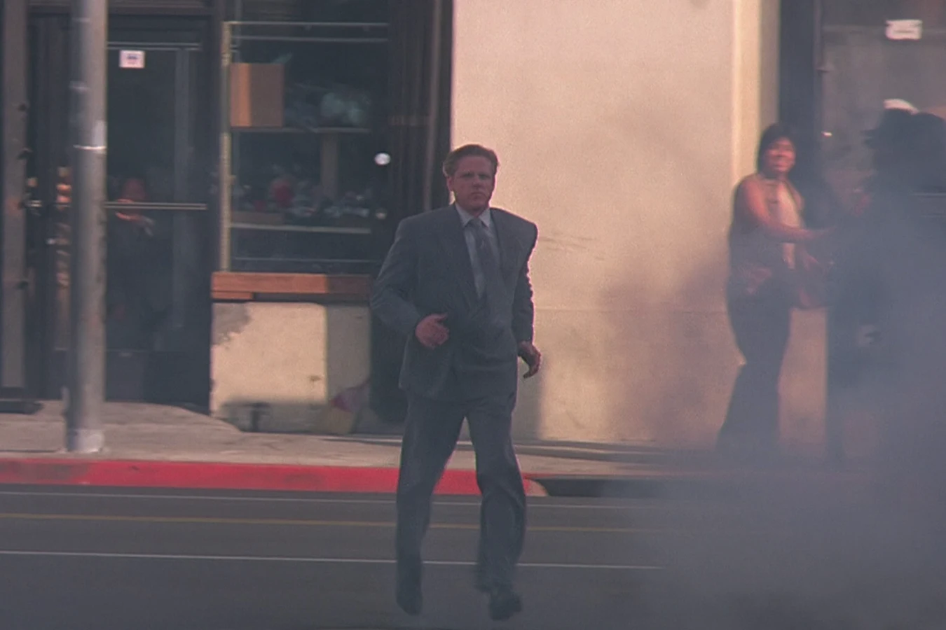 Peter Keyes jogs across a Los Angeles street in a grey suit in Predator 2