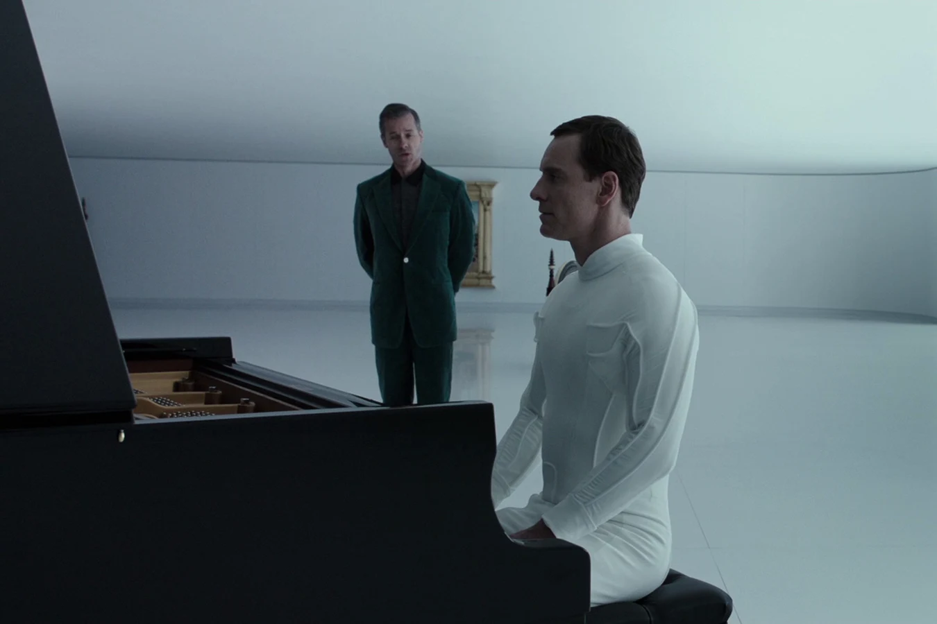 David at a Steinway while Peter Weyland stands behind him in a green suit, in Alien: Covenant