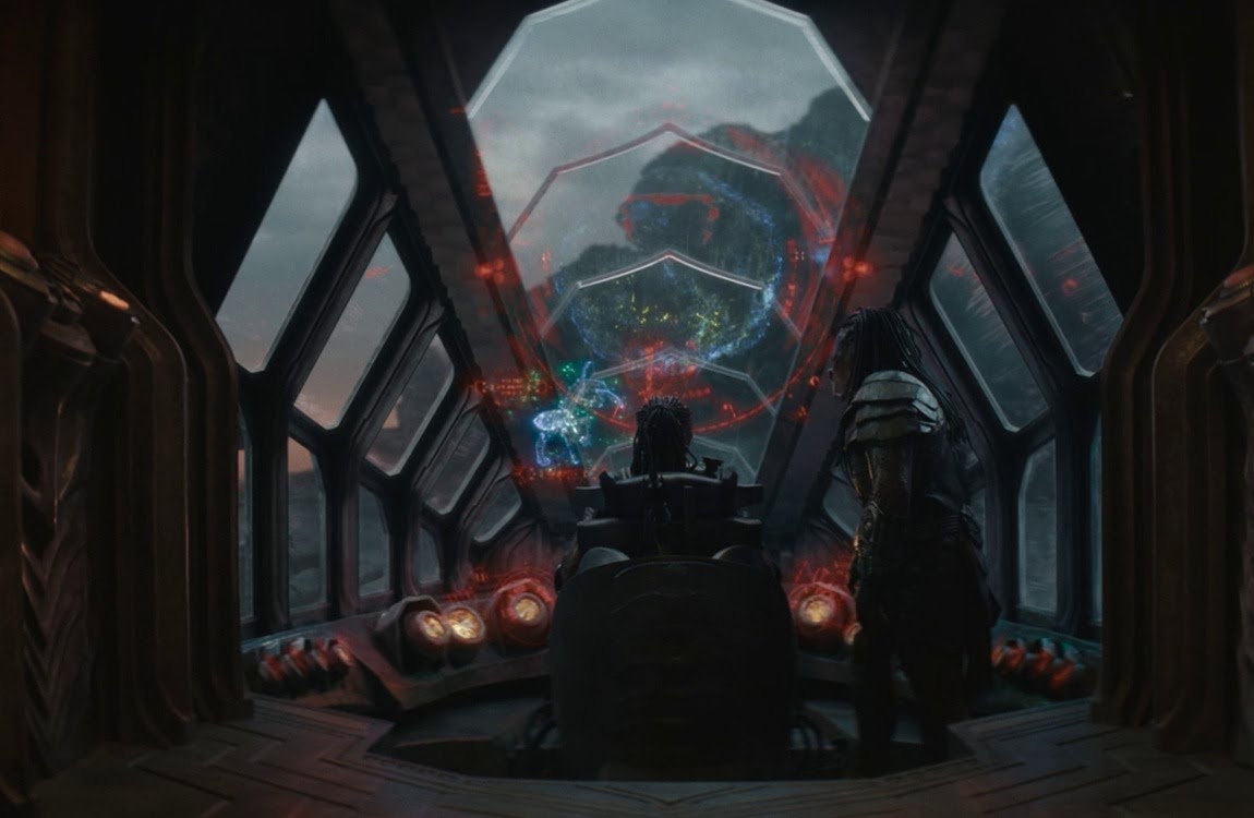 Dek and Kwei viewing a blue planet hologram with a horse-like creature or Drukathi projection inside Kwei's ship in Predator: Badlands