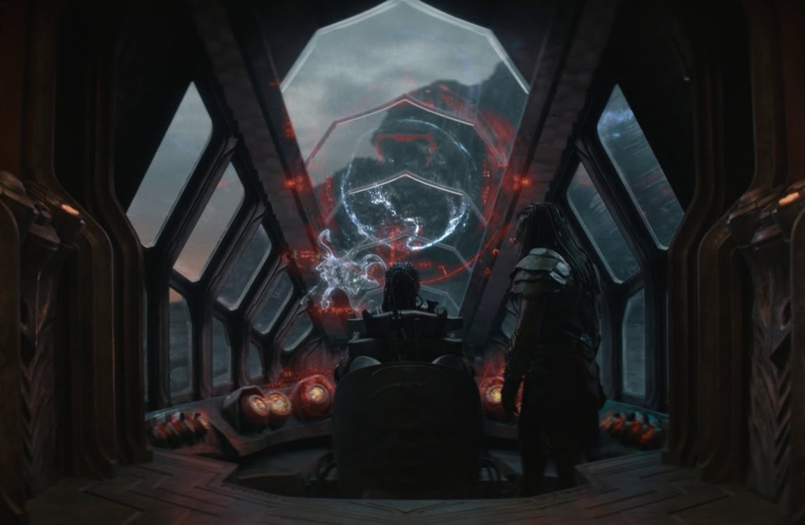 Dek and Kwei viewing a white planet hologram with a tentacled creature projection inside Kwei's ship in Predator: Badlands