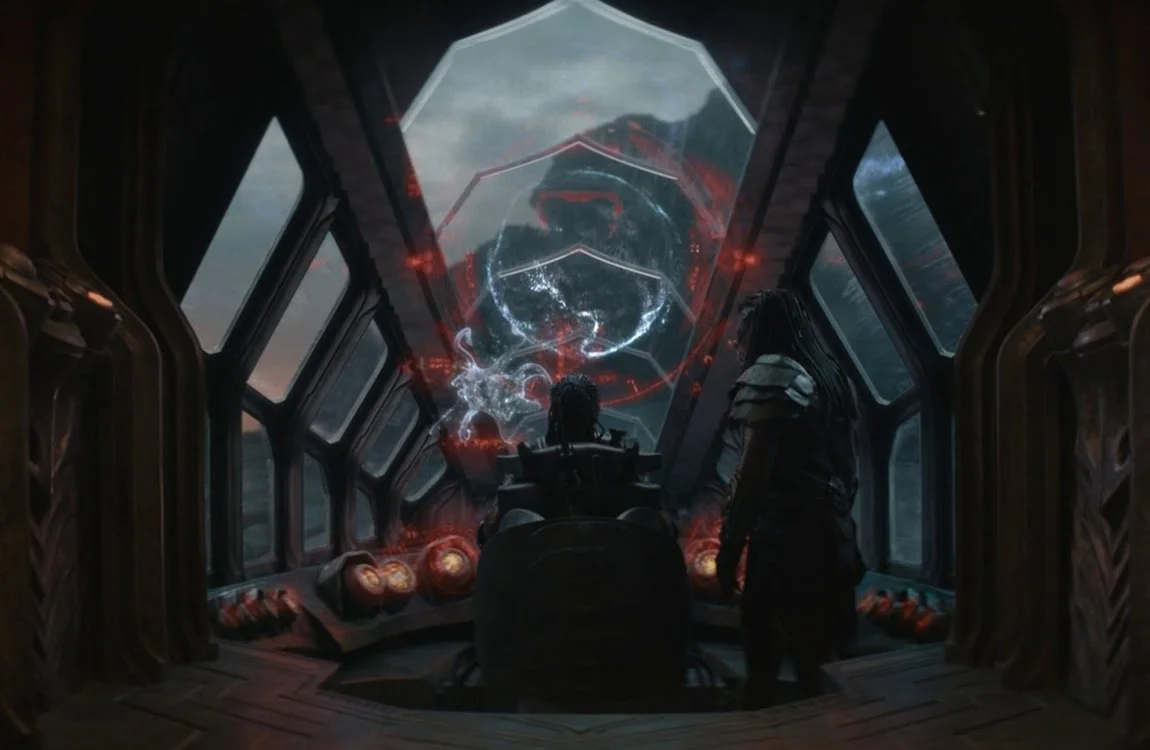 Dek and Kwei viewing a white planet hologram with a tentacled creature projection inside Kwei's ship in Predator: Badlands