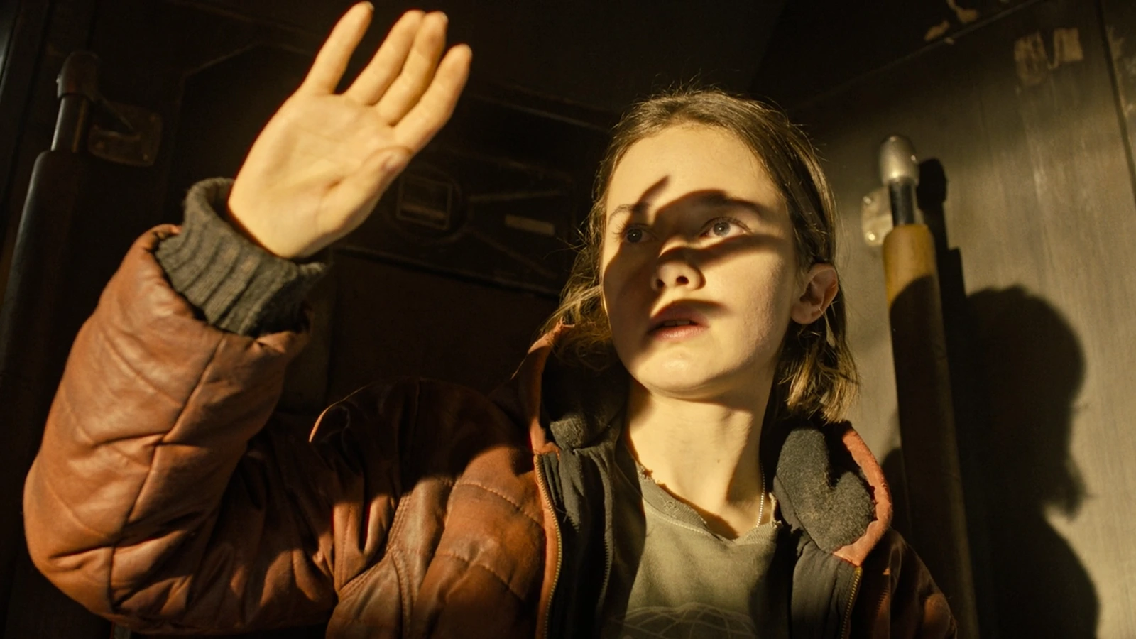 Rain Carradine raises a hand in a brown jacket aboard the Corbelan IV